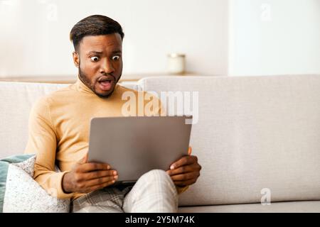 Shocked Black Guy Looking At Laptop Working At Home Stock Photo