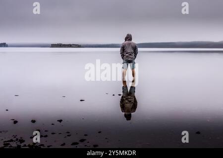 Man standing in the water of Lochindorb in Scotland on a very misty and still morning looking out to the island with the castle Stock Photo