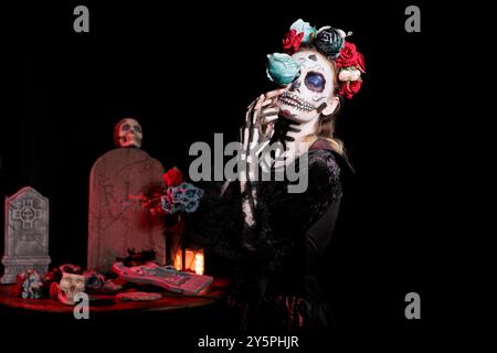 Woman with eyes closed posing with flower for Day of the Dead event to remember the deceased, celebrating their memory. Girl holding blue rose for holiday of remembrance for those who have passed Stock Photo