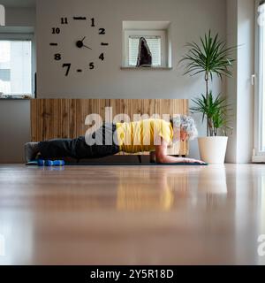 Side view of a senior man doing plank exercise for strong core and body for healthy ageing. On a pilates or yoga mat in a domestic living room. Stock Photo