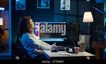 IT specialist working from home, testing and deploying programs using augmented reality. Programmer checking code on computer monitor and AR visualization, sitting at desk chair in apartment, camera A Stock Photo