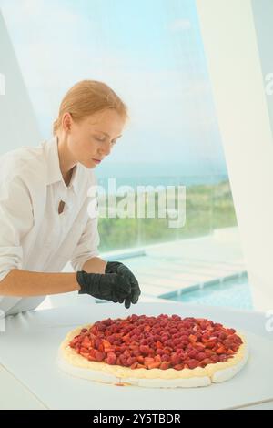 Portrait red haired female pastry chef decorating wedding cake with strawberries Stock Photo