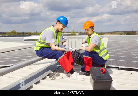 Workers technicians sitting on rooftop and installing solar panels for sustainable energy Stock Photo