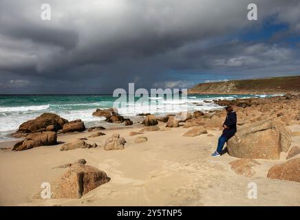 Woman watching an approaching storm on a beach, Sennen Cove, Cornwall. Stock Photo