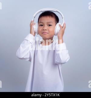 Asian cute boy wearing white and wearing white headphones on his head, Boy standing on white background, Lifestyle of a boy on a white background. Stock Photo