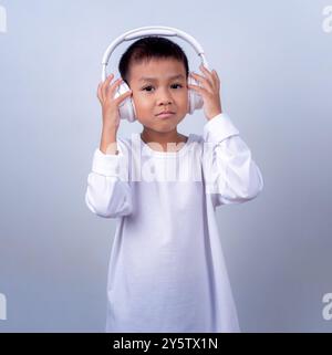 Asian cute boy wearing white and wearing white headphones on his head, Boy standing on white background, Lifestyle of a boy on a white background. Stock Photo