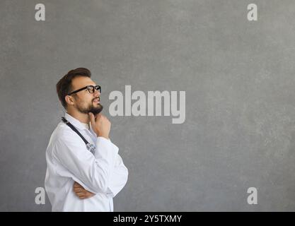 Smiling dreamy male caucasian doctor in white medical uniform look in distance Stock Photo