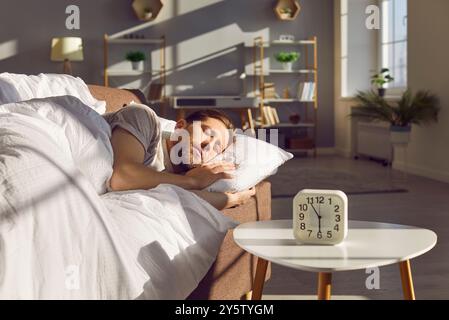 Man Sleeping On Sofa With Alarm Clock In The Morning Stock Photo