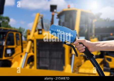 Hand with hydrogen fueling nozzle on a background of fuel cell construction machines. Concept.. Stock Photo