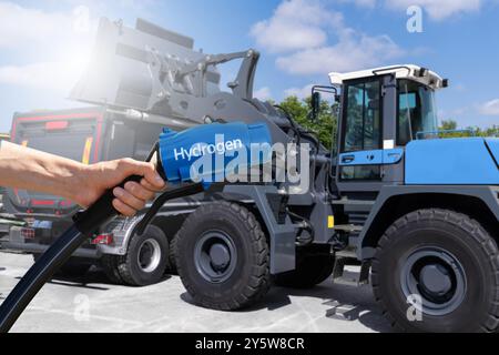 Hand with hydrogen fueling nozzle on a background of fuel cell construction machines. Concept.. Stock Photo