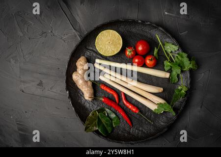 Ingredients for making Tom Yum Kung. Lemongrass, chili pepper, ginger, galangal, lime, cilantro and cherry tomatoes on a black plate against a dark ba Stock Photo