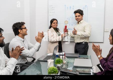A young businessman celebrates winning an award while a happy female colleague congratulates him on job success. They are surrounded by diverse businesses Stock Photo