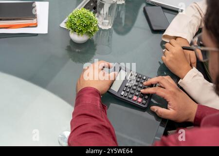 A businessman focused on his budget strategy at an office desk, using a calculator to manage finance represents the intersection of finance, accountin Stock Photo