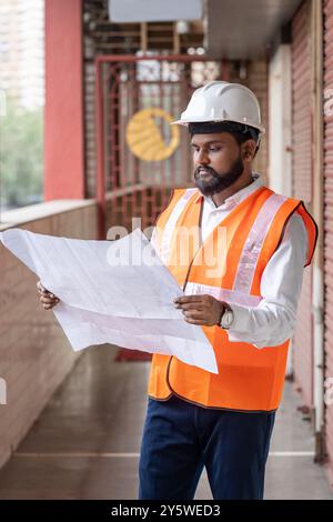 A construction foreman, engineer, manager, and supervisor, dressed in safety gear including hard hats and reflective vests, is deeply engrossed in stu Stock Photo