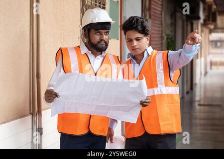 Two dedicated project engineers deeply involved in discussing the site floor plan and deciding on their next steps. Wearing safety gear, they demonstr Stock Photo