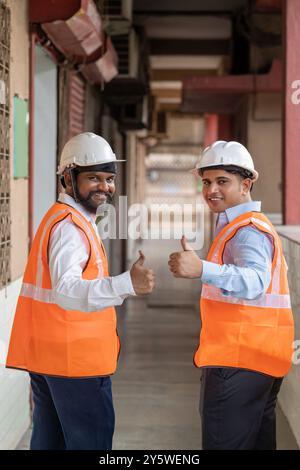 Two warehouse construction workers in a commercial industrial warehouse setting, both giving a thumbs-up and their positive expressions and confident Stock Photo