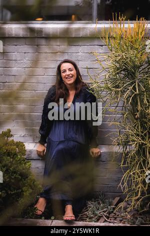 Happy woman sitting in front of a grey brick wall. Stock Photo