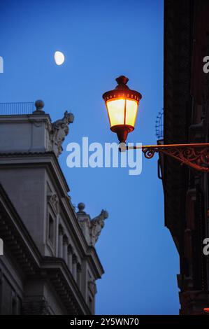 Elegant street lamp illuminates a Roman street under a moonlit sky Stock Photo