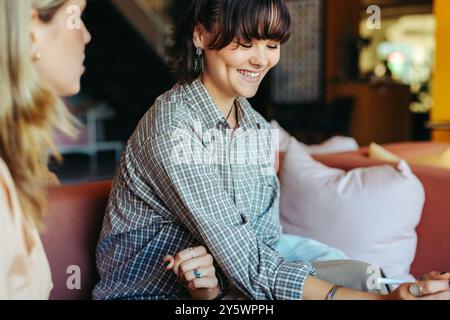 A cheerful student enjoys a conversation with a friend in a relaxed lounge setting, highlighting youthful camaraderie and happiness. Stock Photo
