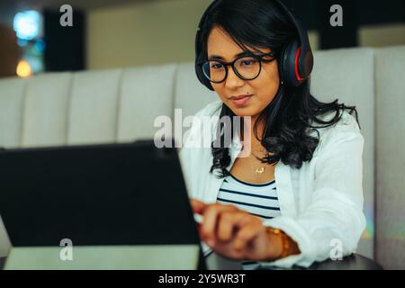 Engaged student using headphones while learning on a tablet in a cozy setting. The image captures focused study and a modern educational experience. Stock Photo