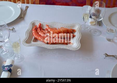 A formal dining table set with plates, glasses, napkins, and a platter of large prawns at the center. Stock Photo