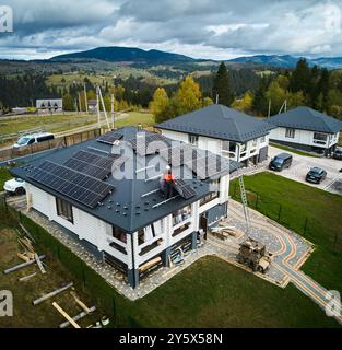 Professional engineers installing solar battery on a roof of big wooden house. Drone view of solar panels installation in mountains. Green electricity concept. Stock Photo