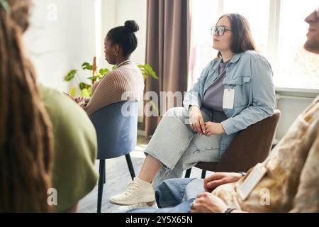Diverse group of people sitting in modern classroom, engaging in collaborative learning environment, with natural light streaming through large windows Stock Photo