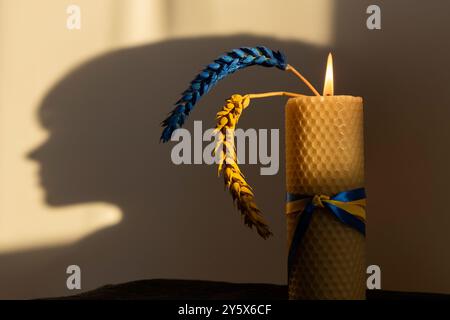 burning candle, two ears of wheat, painted yellow-blue against background of shadow of silhouette of a child head Stock Photo