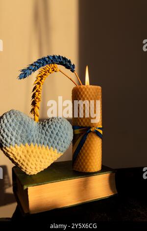 burning candle, two ears of wheat, painted yellow-blue, and a knitted heart. Stock Photo