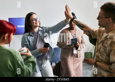 Group of colleagues engaging in lively discussion, diverse team members sharing ideas and celebrating success with high-five. Laughter and joy emanating from the team during the meeting Stock Photo