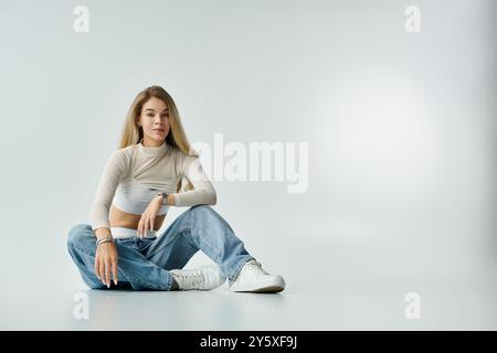 A confident young woman sits casually on the floor in stylish, comfy clothes. Stock Photo