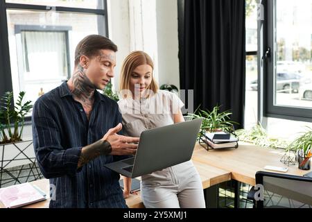 Two young coworkers engage in a discussion while working on a laptop in a modern office. Stock Photo
