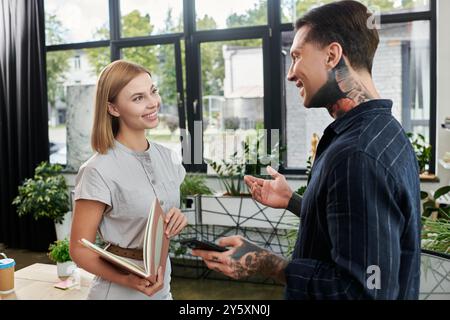 A friendly exchange unfolds between two colleagues in a bright, plant filled workspace. Stock Photo