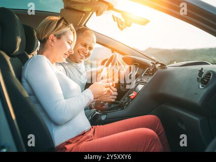Happy smiling two young adulds couple using smartphone navigation inside car during auto jorney.They are laughing during road trip. Family, couples re Stock Photo