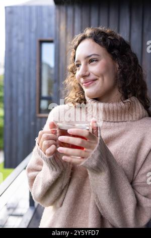 Smiling woman holding cup of tea, enjoying relaxing moment on balcony Stock Photo