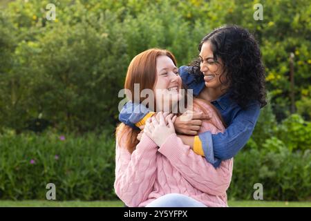 Hugging and laughing, two women friends enjoying time together outdoors in park Stock Photo