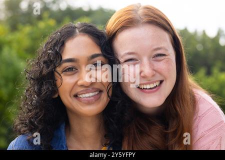 Smiling diverse women friends enjoying outdoor hangout, embracing and looking at camera Stock Photo