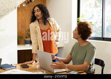 Discussing project, two women collaborating with laptop and documents in office Stock Photo