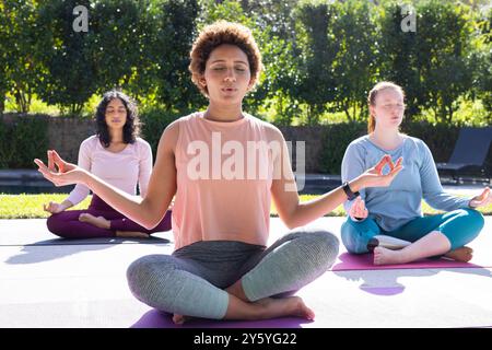 Meditating on yoga mats, diverse women friends practicing mindfulness outdoors together Stock Photo