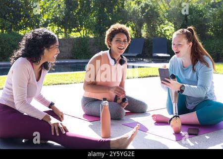 Sitting on yoga mats, diverse women friends chatting and laughing outdoors Stock Photo