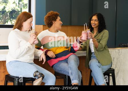 Drinking smoothies, diverse friends sitting and chatting in modern kitchen Stock Photo