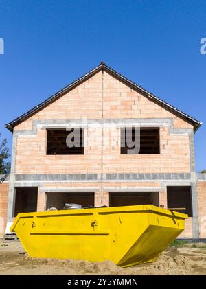 Unfinished brick house with construction skip in front Stock Photo