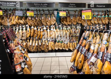 A range of Iberian hams on sale in a supermarket in Spain. Jamón ibérico, leg of pork varieties. Hanging in a store. Cured leg of pork display on sale Stock Photo