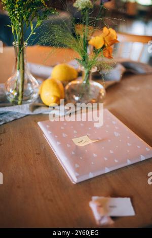Gift Wrapped in Pink Paper with Lemons and Floral Vase Decor on Wooden Table Stock Photo