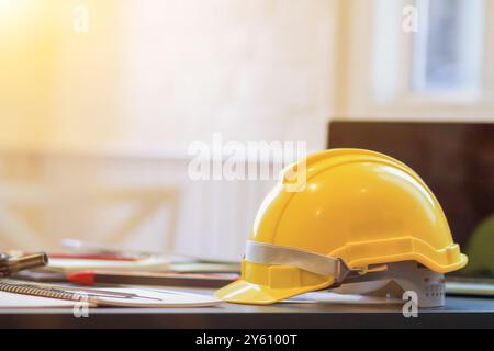 Yellow hard plastic safety helmets sit on work desks in office intended for architects and engineers to wear when entering construction sites as safet Stock Photo
