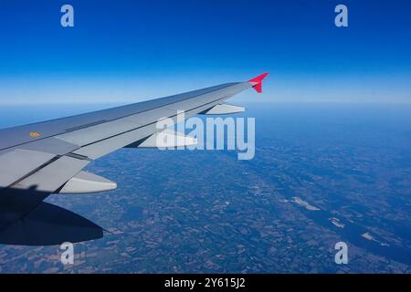 View of the airplane wing in clear weather with blue sky and sunshine. Stock Photo