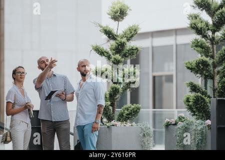 Group of three diverse professionals collaborating outdoors with green plants and modern architecture. Stock Photo