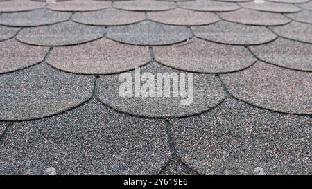 fragment of soft tile roof covering with granular texture and rounded edge lines in gray-red shade, background industrial textured surface Stock Photo