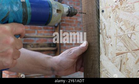 close up of male working hands with drill making hole in wooden material structure, building cage for domestic quails using drilling and fasteners Stock Photo