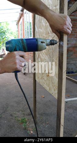 drilling holes in poultry cage structure with old drill in male hands, constructing quail cage using hand tool Stock Photo
